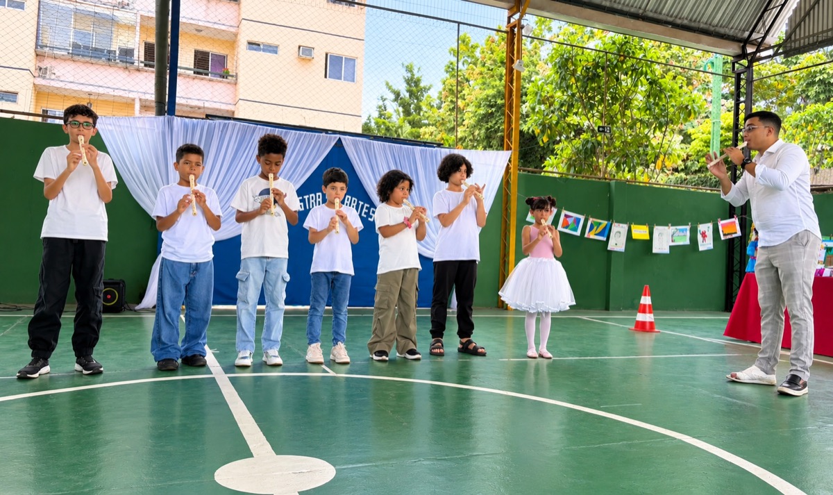 Alunos tocando flauta doce na quadra, acompanhados pelo professor